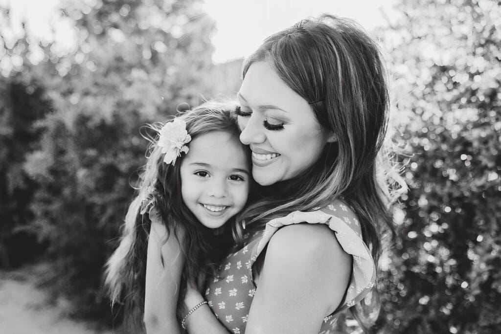 black and white image of mom smiling while holding her daughter close
