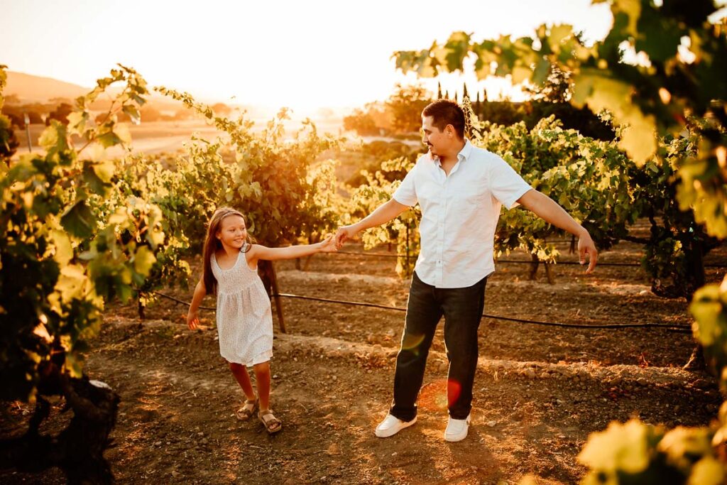 father and daughter dancing in a vineyard at sunset