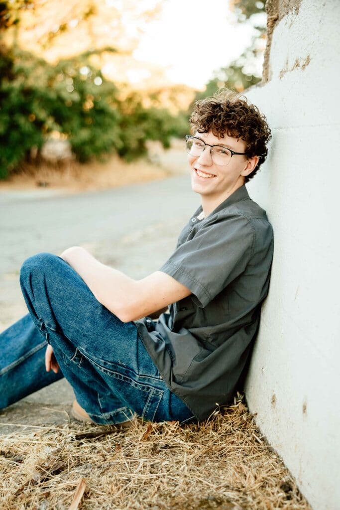 up close portrait of a senior boy smiling and sitting against a wall