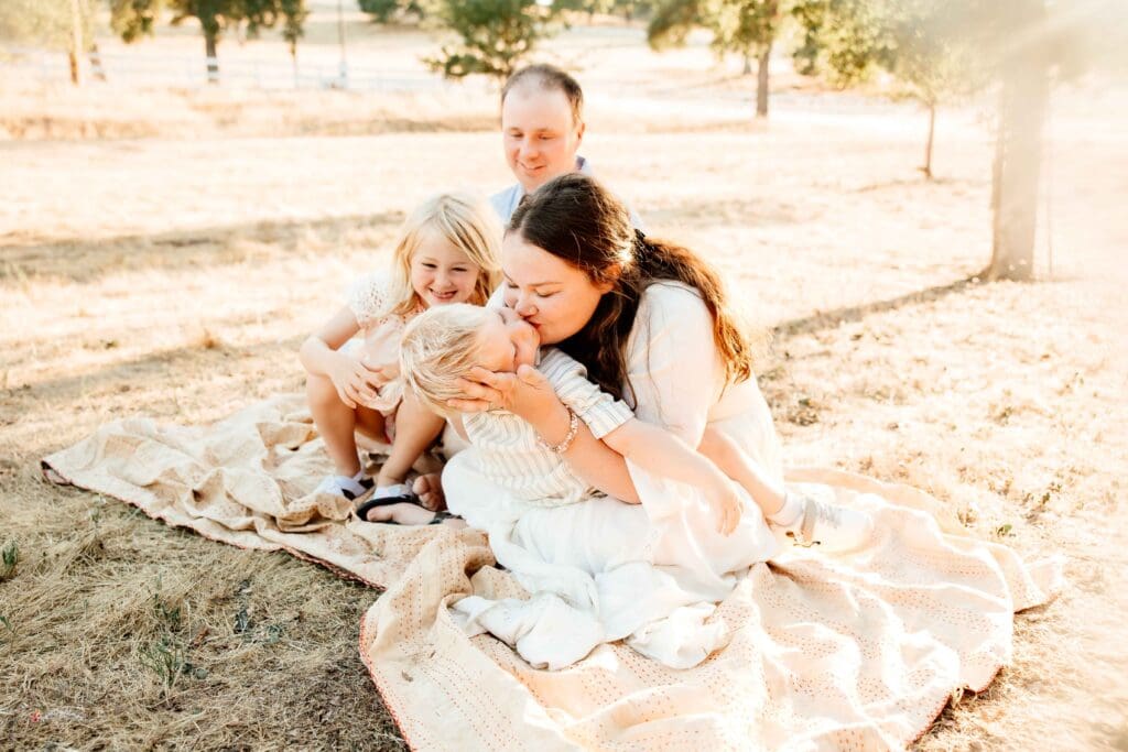 Family of 4 sitting on a blanket and being playful
