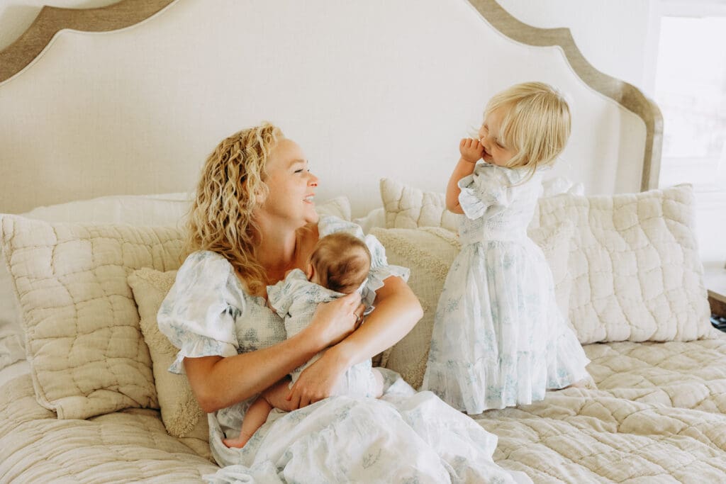 Mother on the bed holding her baby and looking adoringly at her young daughter