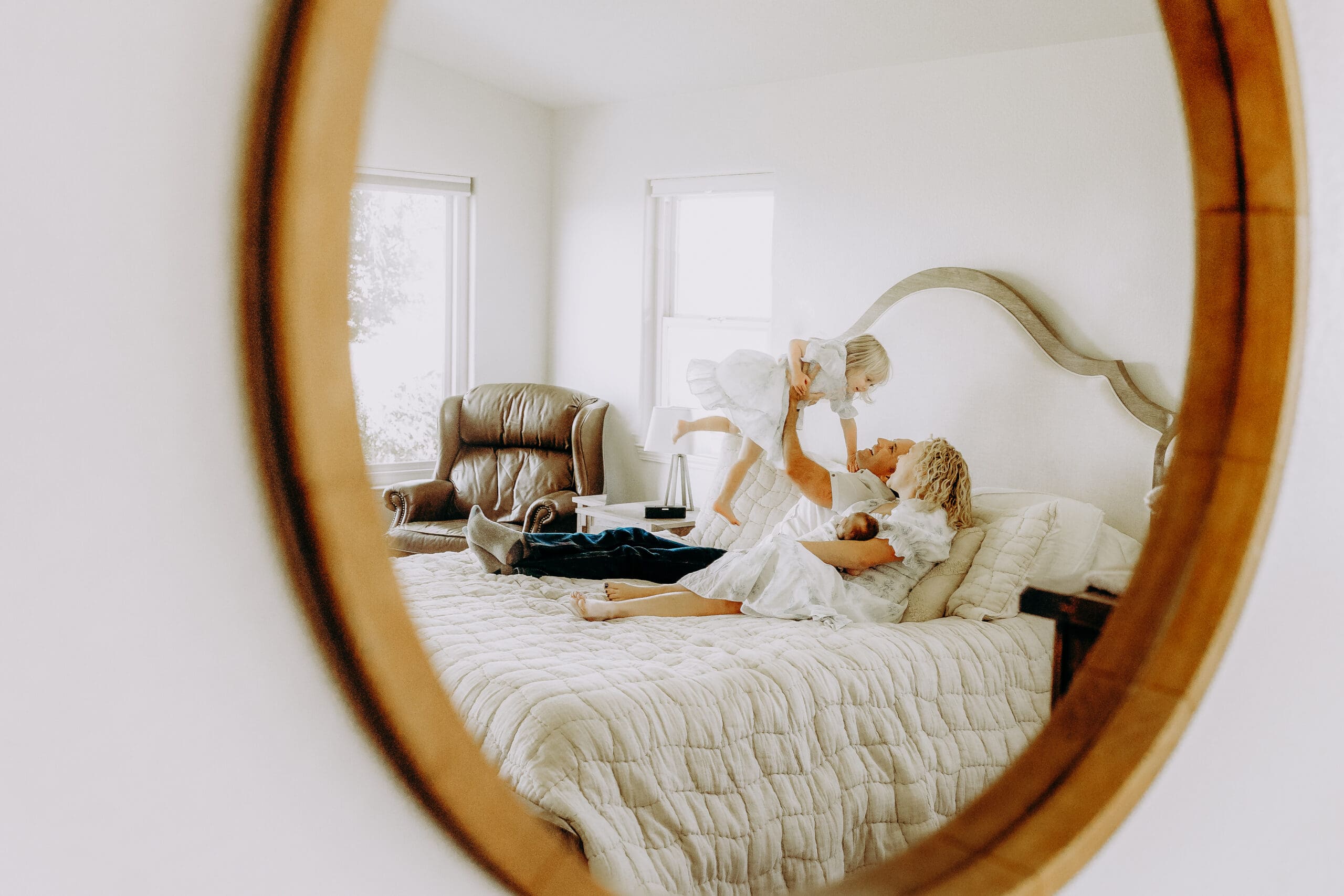 Family of 4 on their bed playing and laughing in an in-home lifestyle photo session