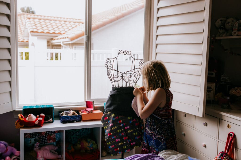 a young girl in her room dressing a mannequin
