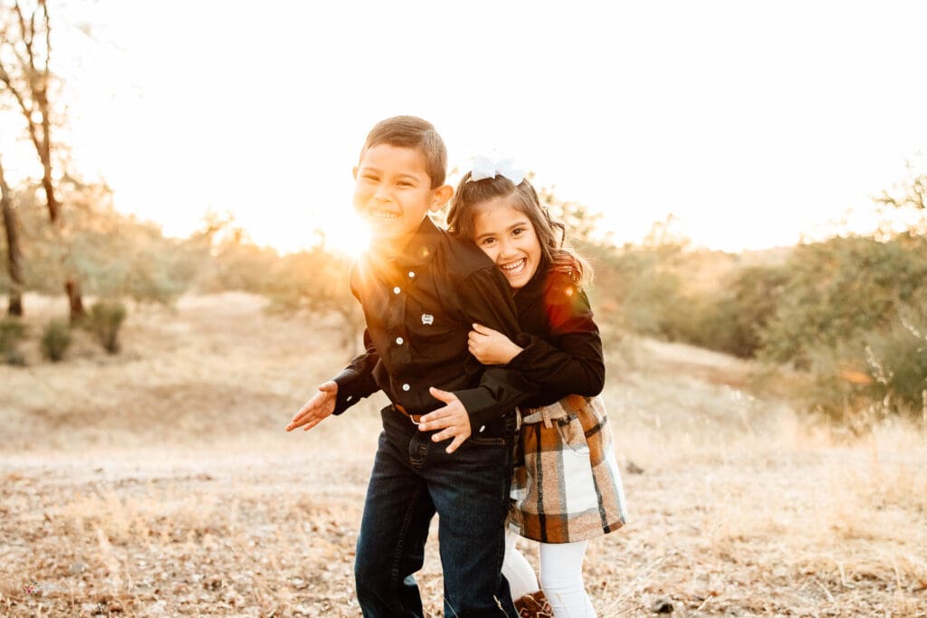 Sunlit in=mage of a young brother and sister embracing and laughing